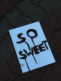 Blue sign with 'SO SWEET' text on a dark textured surface