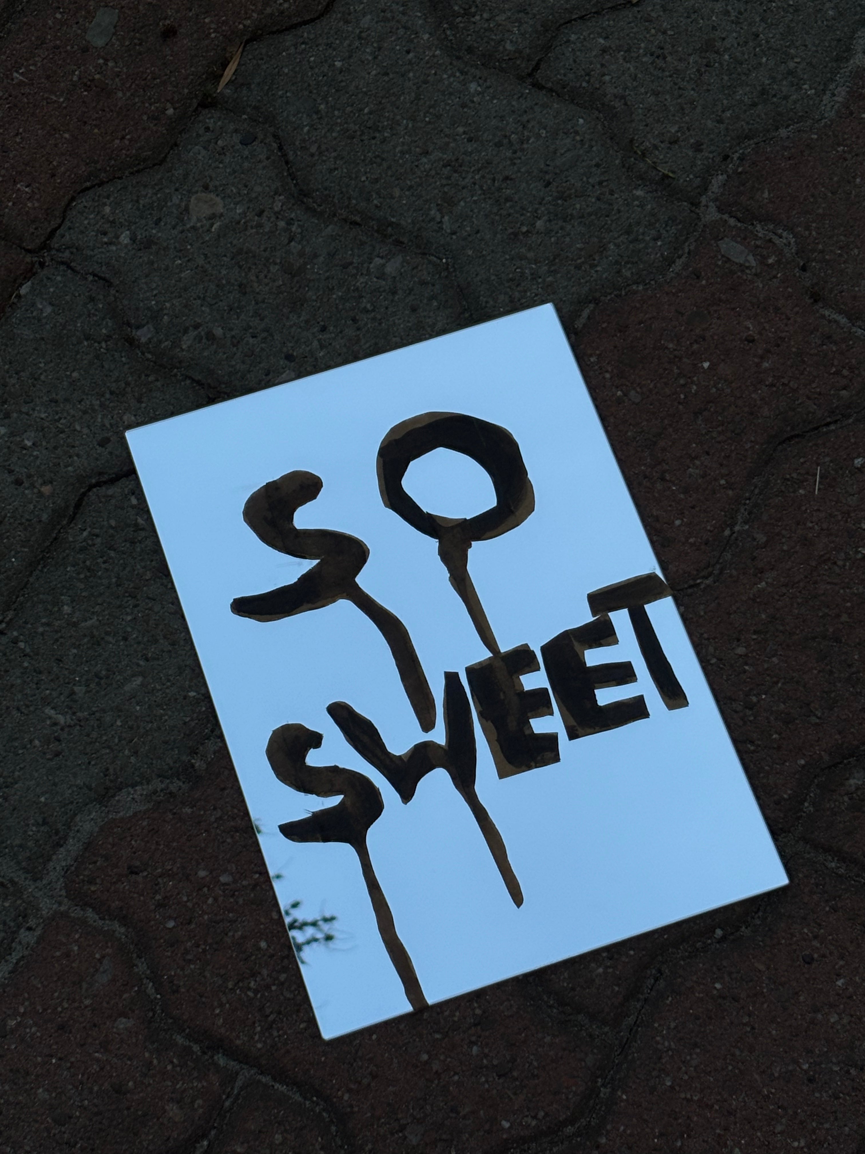Blue sign with 'SO SWEET' text on a dark textured surface