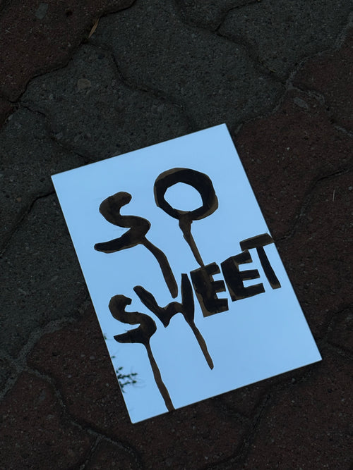 Blue sign with 'SO SWEET' text on a dark textured surface